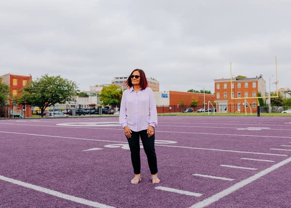 A woman in a light purple shirt stands on a slightly darker purple football field.