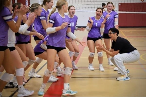 A coach cheers in front of a group of youth volleyball players