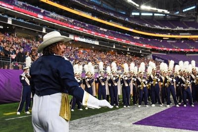 A marching band performs on the field of a football stadium.