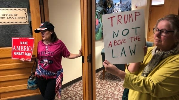 Two women are in front of the mayor's office, holding signs. 