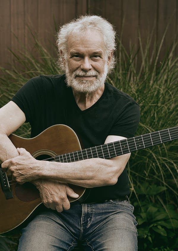 A bearded man with a guitar poses for a portrait