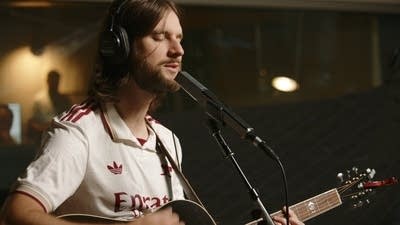 A musician in an Arsenal shirt sings and plays guitar in a recording studio