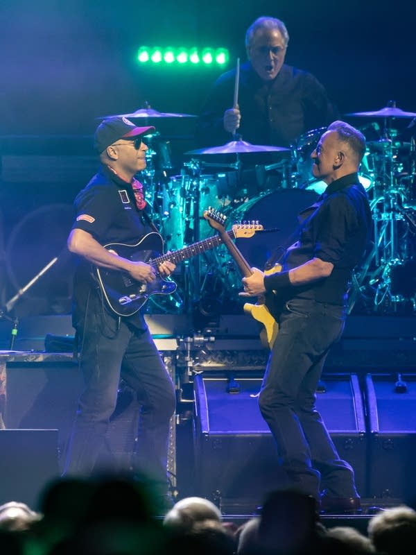 Three musicians performing onstage during an arena concert