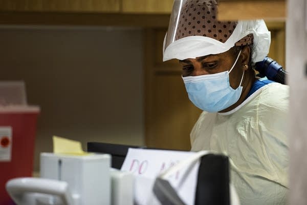A health care worker wears a mask as she works outside a patient room.