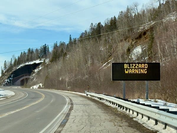 A sign near the highway reads "Blizzard Warning."