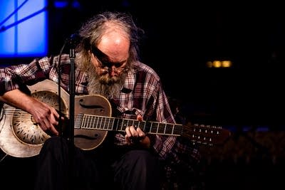 A musician plays a resonator guitar onstage at a music festival