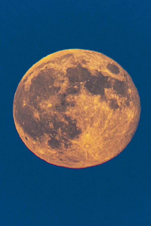 A bright orange full moon rises over a city against a dark blue sky.