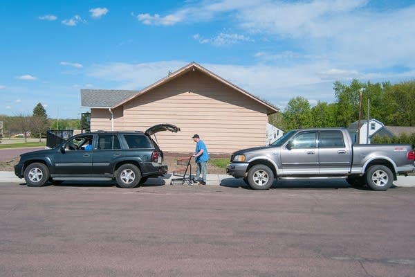 A person pushing a cart between a line of cars. 