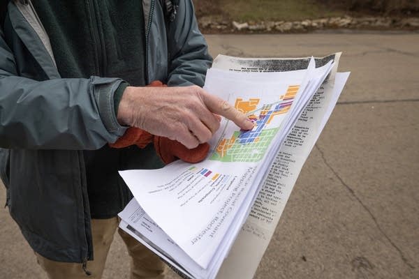 A person looks at a packet of paper while walking through a neighborhood.