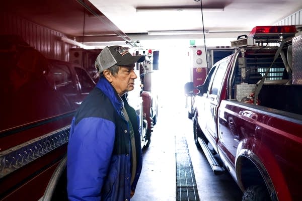 A man walks between a fire engine and a red pickup truck in a garage.