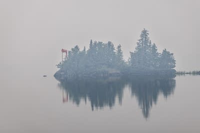 a small island of trees is seen through smoke over a lake