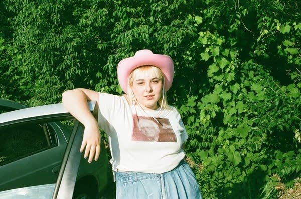 A woman stands outside an open car door on a summer day