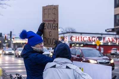 A protester holds a cardboard sign reading, "FFS. Enough is enough."