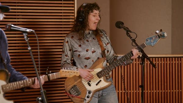 A woman sings and plays bass in a recording studio