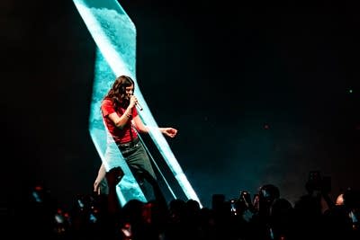 A musician sings and dances onstage in a large music venue
