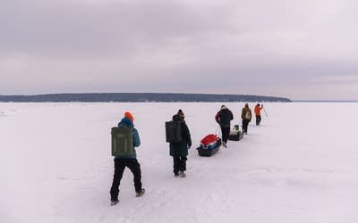 People walk in a line on a frozen lake.