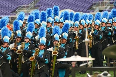 A marching band performs on the field of a football stadium.