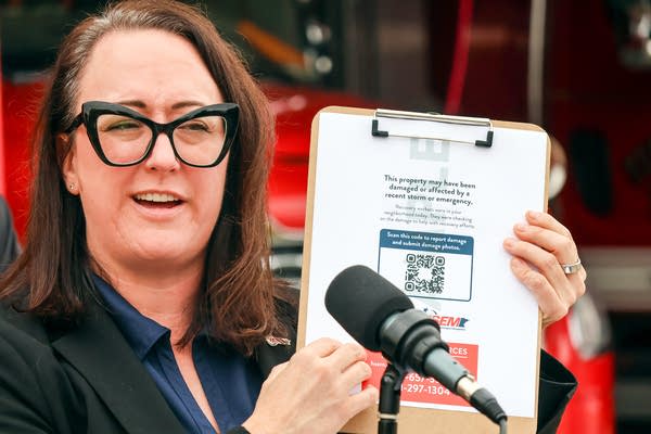 A woman holds up a clipboard with a paper document showing a QR code on it.