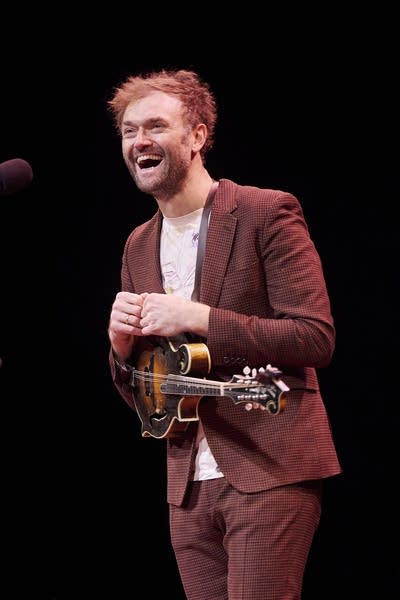 A musician with a mandolin laughs while performing onstage