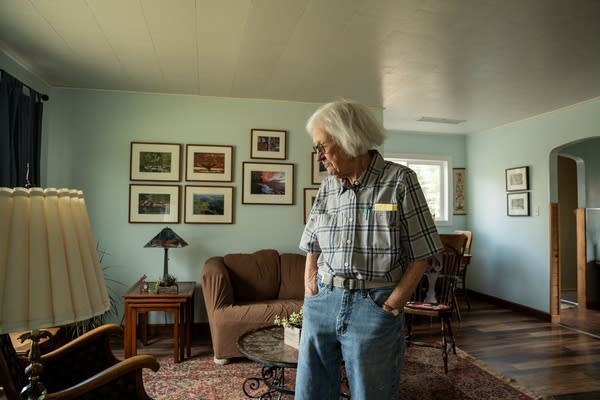 A woman stands and looks downward in the middle of her living room.