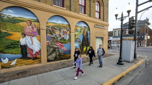 A family walks past a mural depicting the history of Sauk Centre.