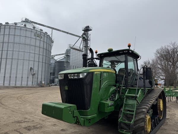 A green tractor in front of grain bins
