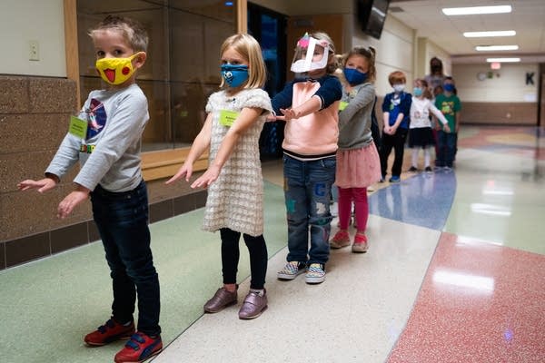 Students in masks walk in a line with their arms out in front of them.