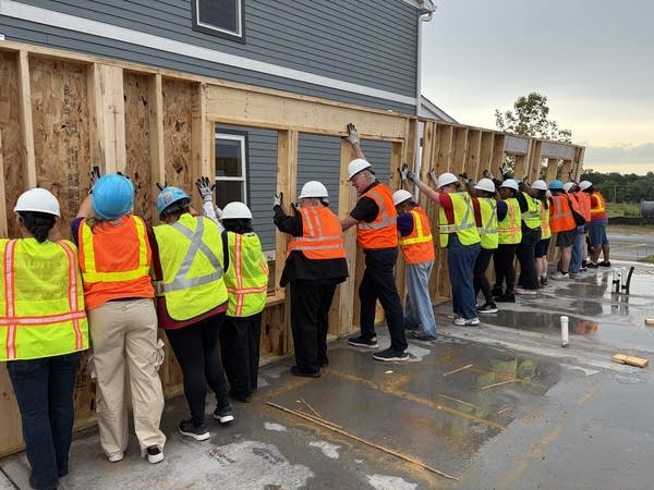 Peoplein vests holding up a wall on a house