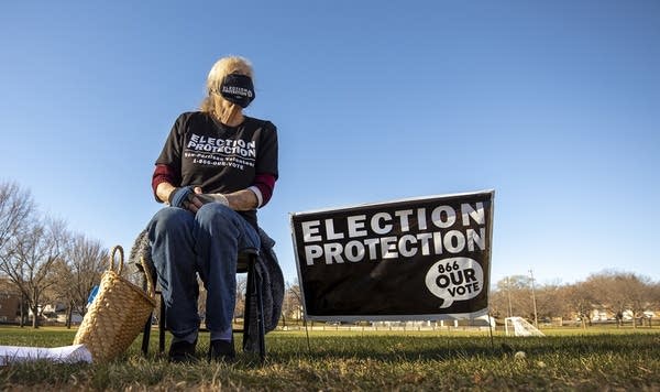 A person sitting in a chair beside a sign that reads "election protection"