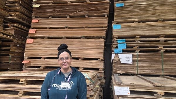 Stephanie Koste in front of a stack of wood veneers at the Manthei Wood Products factory in Petoskey, Michigan, where she's worked since leaving rehab.