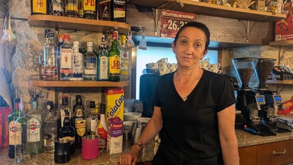 A woman with black hair stands behind a rustic bar