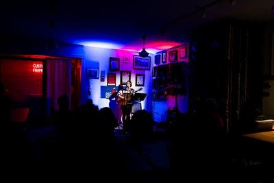 A musician sings and plays guitar onstage in a small venue