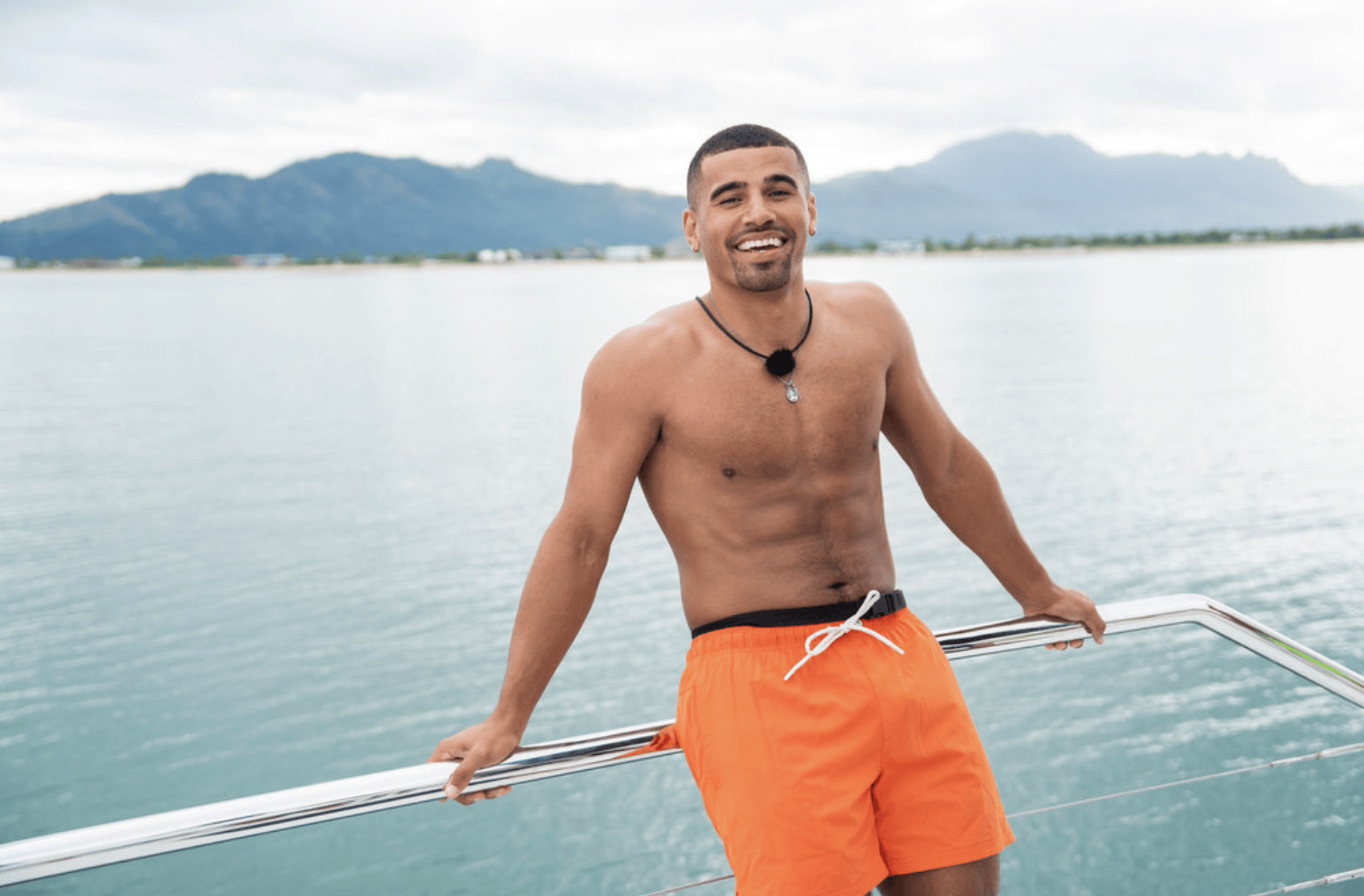 Man in swim shorts smiles from a boat
