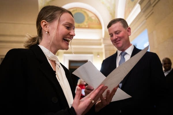 Two people hold white print outs