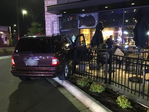 An SUV sits on top of a curb and stuck on a fence in front of a storefront