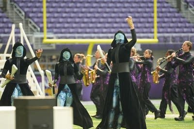 A marching band performs on the field of a football stadium.