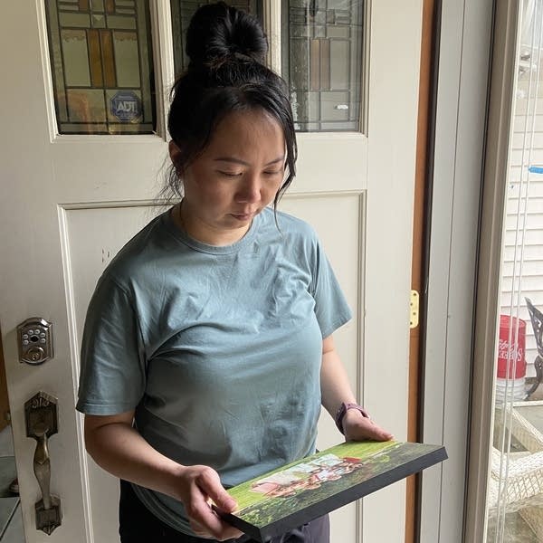 A woman stands in a doorway looking down at a photo. 