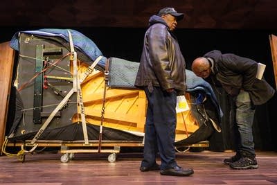 Two men stand next to a grand piano