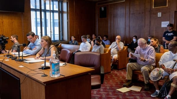 A room full of people listen to someone speak into a microphone