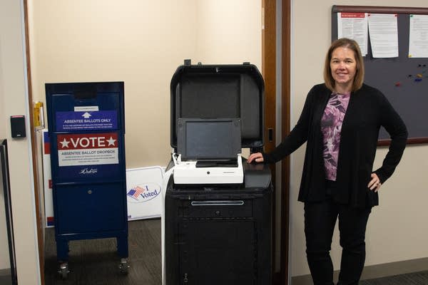 A woman stands next to a voting machine.