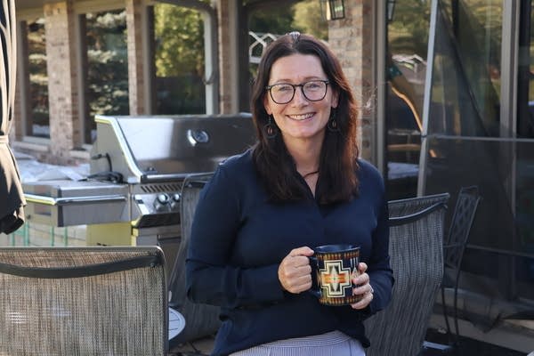A woman smiles while holding a cup of coffee