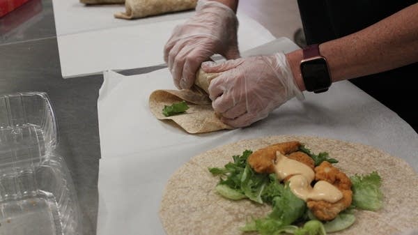 A school nutrition employee rolls tortillas filled with lettuce, chicken, and sauce