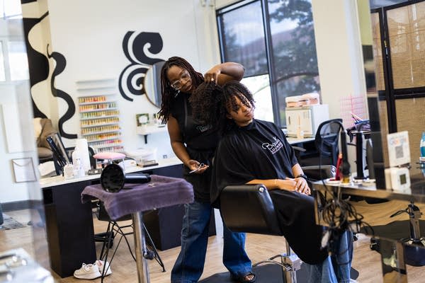 A Black woman styles a woman's hair
