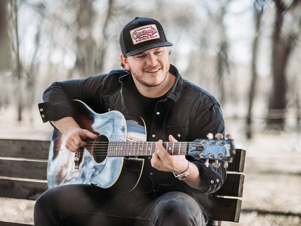 A man plays a guitar on a park bench