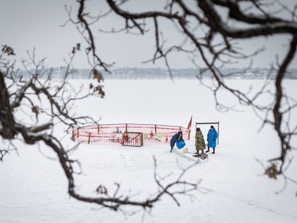 Tree branches frame three people on a frozen lake