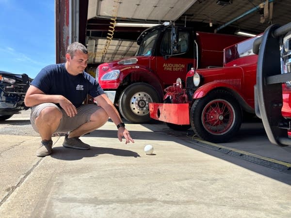 A man kneels down and places a ball on the ground.