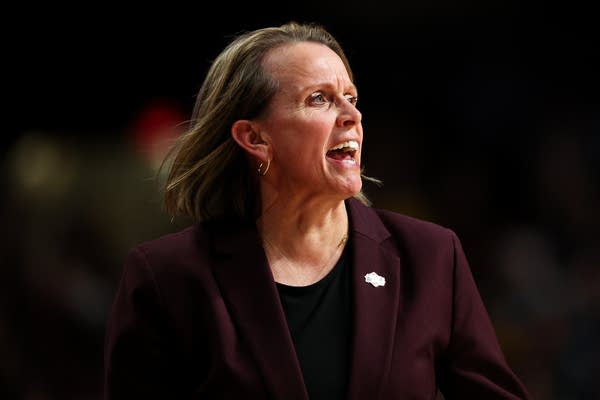 A woman in a burgundy blazer yells to the side.