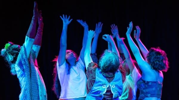 A group of people on stage reach up with their arms, in blue lights.