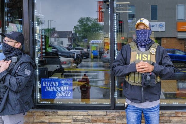 An agent stands with their face covered