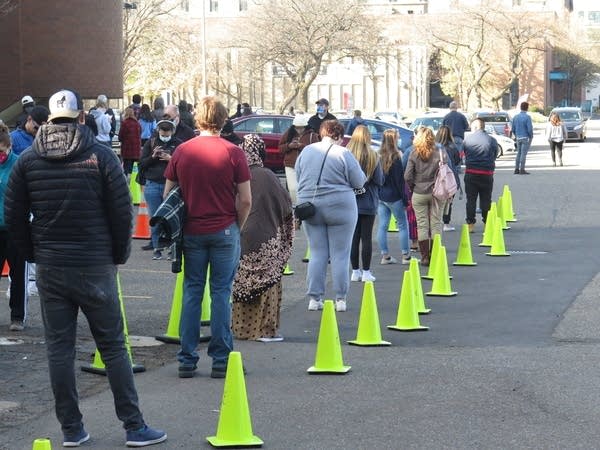 Cones and people line up in a parking lot outside of a building.